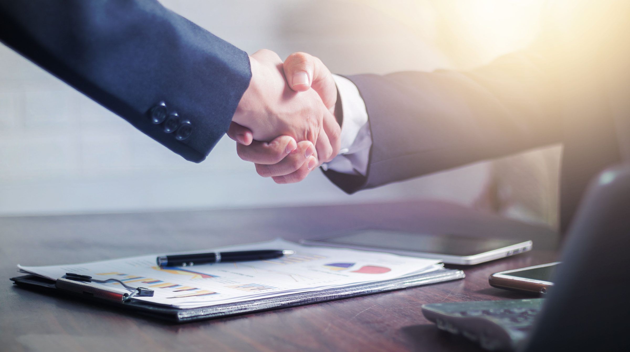 Two business partners shaking hands over documents
